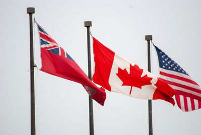 Low angle view of us and canadian flags against sky