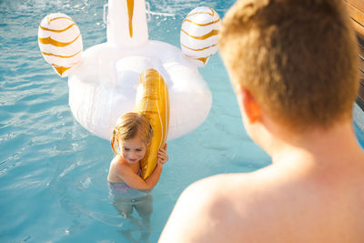 Rear view of girl swimming in pool. father looking after kid