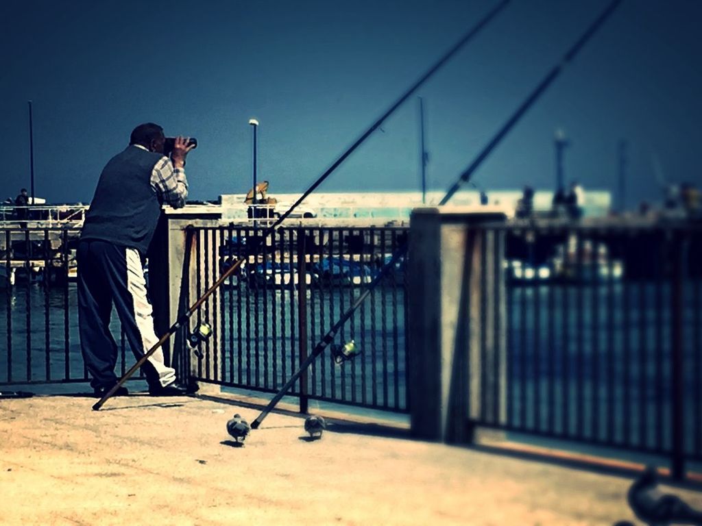 lifestyles, full length, leisure activity, men, railing, built structure, clear sky, rear view, sea, standing, casual clothing, architecture, blue, walking, building exterior, sky, copy space