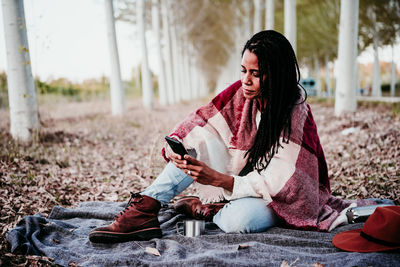 Full length of woman using smart phone while sitting amidst trees