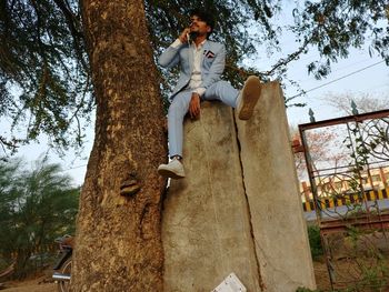 Low angle view of man sitting on tree trunk