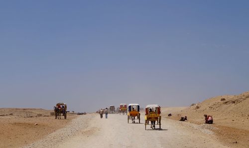 People riding horses in desert against clear sky