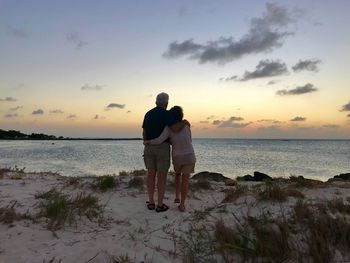 Rear view of senior couple standing at beach during sunset