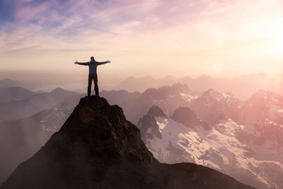 Silhouette man standing on rock against sky during sunset