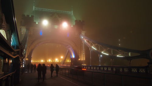 People walking on illuminated bridge at night