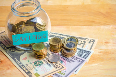 High angle view of coins and paper currency with glass jar on wooden table