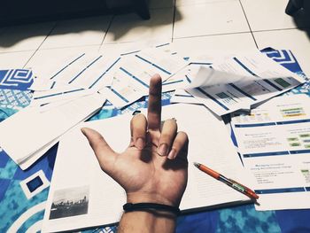 Cropped hand of man showing obscene gesture over documents at home