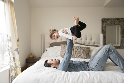 Playful father lifting daughter while on bed at home
