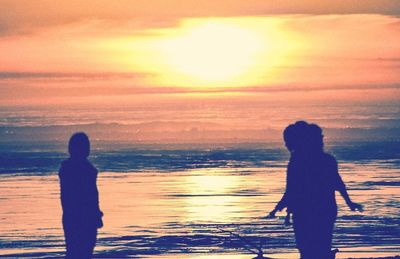 Rear view of silhouette woman standing at beach during sunset