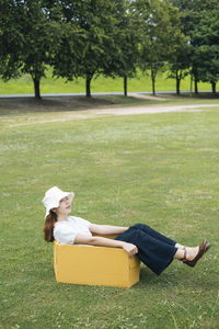 Full length of woman sitting on box in grass