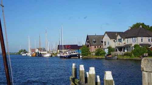 Sailboats moored on river by buildings against blue sky