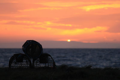 Silhouette fish traps on field against orange sky during sunset