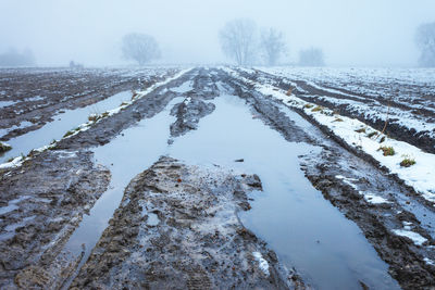 Water and mud on dirt road and fields on a foggy day, february afternoon