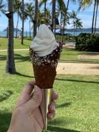 Hand holding ice cream cone against trees