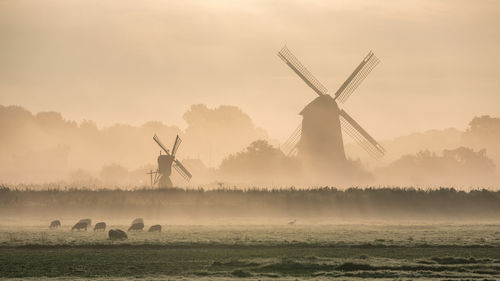 Traditional windmill on field against sky during sunset