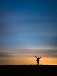 Silhouette man standing on field against sky during sunset