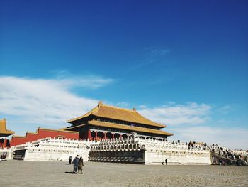 People at historical building against blue sky