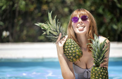 Portrait of young woman wearing sunglasses holding pineapples