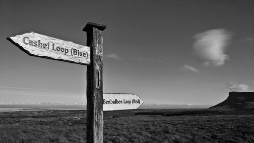 Information sign on wooden post on field against sky