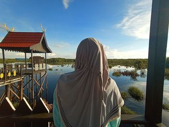 Rear view of woman by lake against sky