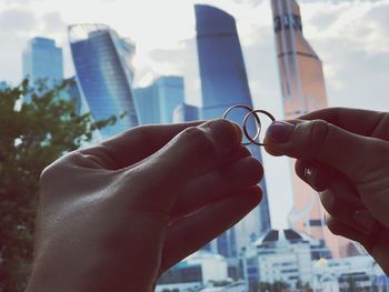 Cropped hands holding rings against buildings in city