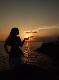 Silhouette woman looking at sea against sky during sunset
