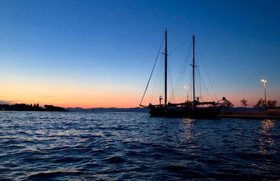 Sailboats sailing in sea against clear sky during sunset