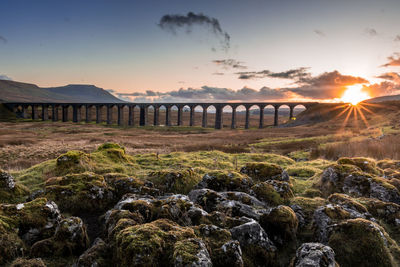 Bridge over rocks against sky during sunset