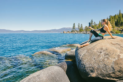 Young woman sitting by lake tahoe reading a kindle book during the day