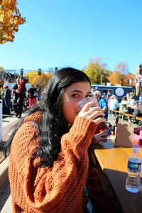 Young woman drinking water against sky