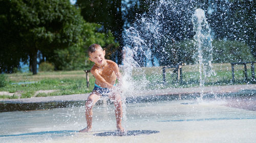 Excited boy of seven years having fun between water jets, in fountain, run around, sprinkle, have