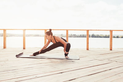 Full length of woman exercising against railing and sky