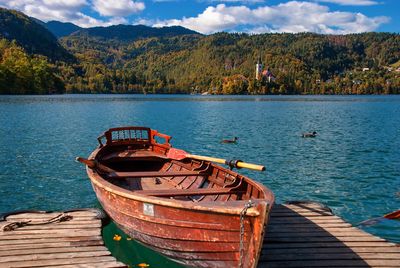 Boat moored on pier by lake against sky