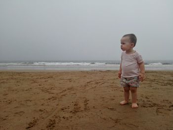 Boy standing on beach against sky