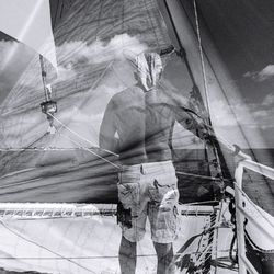 Double exposure of shirtless man in boat with mast