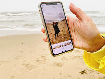 Midsection of man holding mobile phone at beach