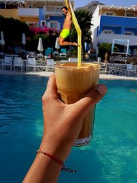 Hand holding drink by swimming pool