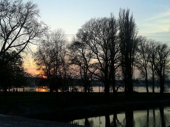 Silhouette bare trees by lake against sky during sunset