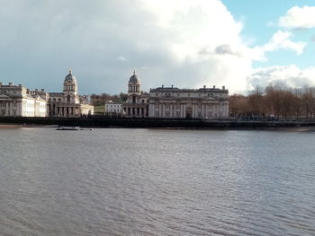 View of buildings by river against cloudy sky