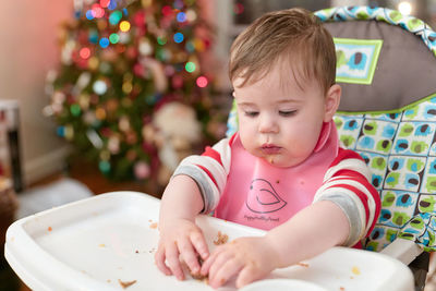 Little boy toddler eating in his high chair in front of the christmas tree