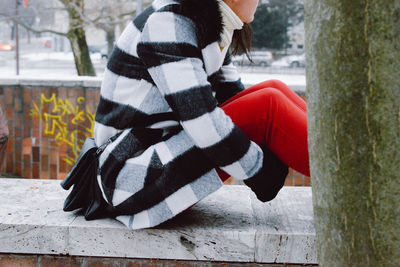 Midsection of woman sitting on retaining wall during winter