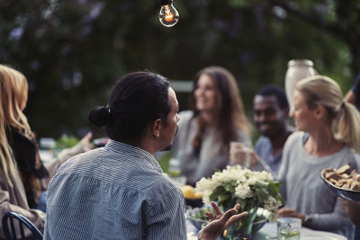 Rear view of man sitting at dining table with friends at outdoor dinner party