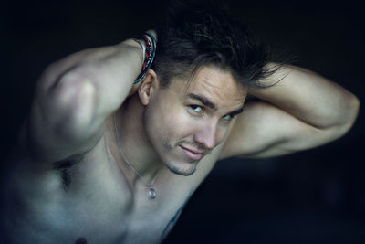 Close-up of shirtless young man against black background