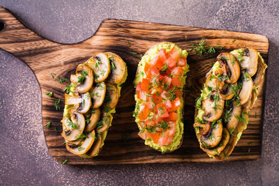 Close up of sandwiches with avocado, fried champignons, tomatoes and herbs on rye bread top view