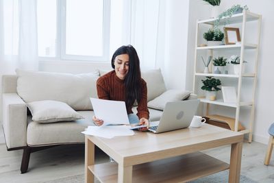 Young woman using laptop while sitting on sofa at home