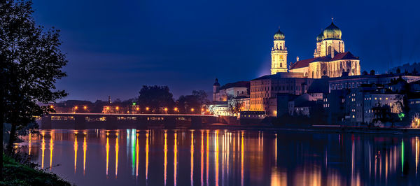 Illuminated buildings by river against sky at dusk