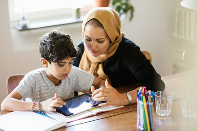 Mother and son using digital tablet while studying at home