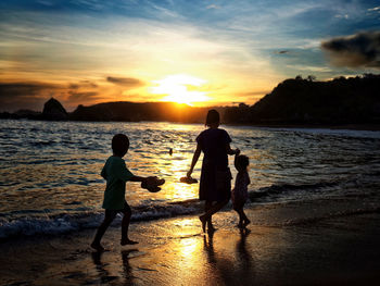 Silhouette people on beach against sky during sunset