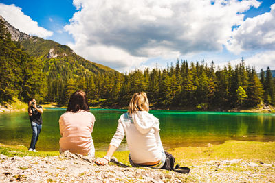 Rear view of women sitting by lake against sky