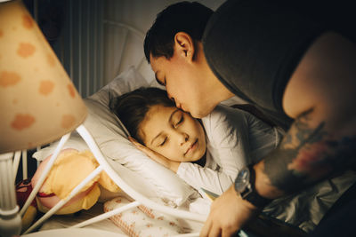 Father kissing daughter while sleeping in bed at home